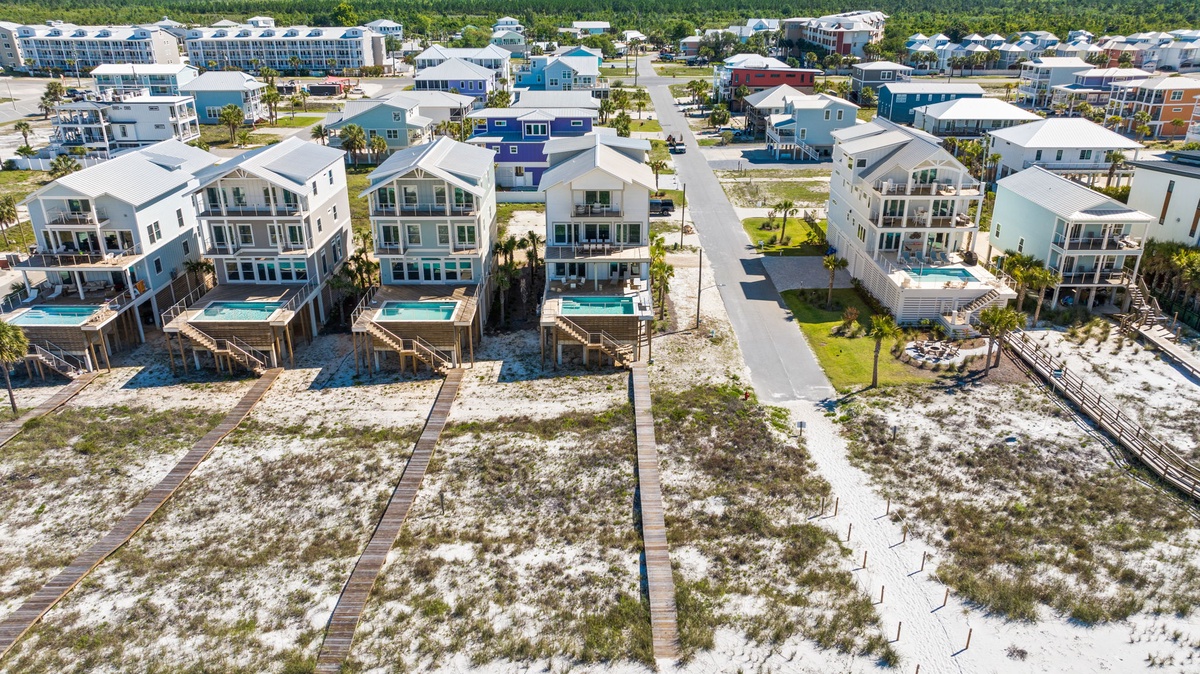 Aerial view of a coastal vacation rental community featuring modern beach houses with private pools, surrounded by white sandy shores and tropical palms, just steps from the Gulf coast.