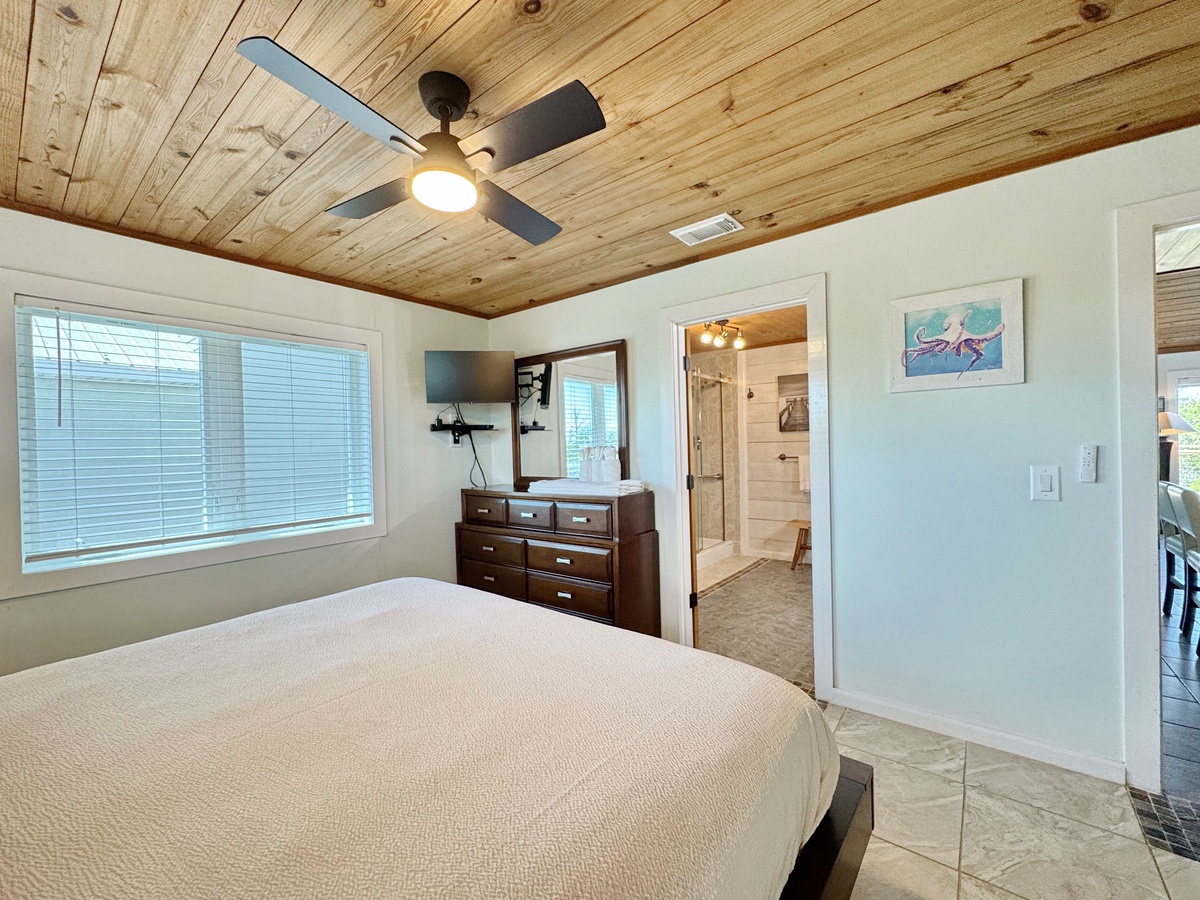 Rest easy in this serene bedroom featuring a stunning wood-planked ceiling, cozy bedding, and natural light streaming through large windows.