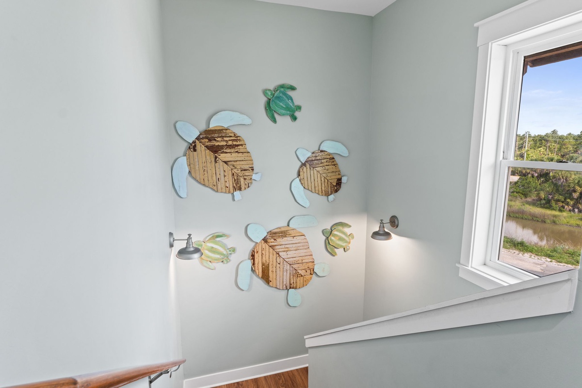 Charming sea turtle wall art adds coastal flair to your bedroom, while large windows frame tranquil water views, creating a peaceful retreat.