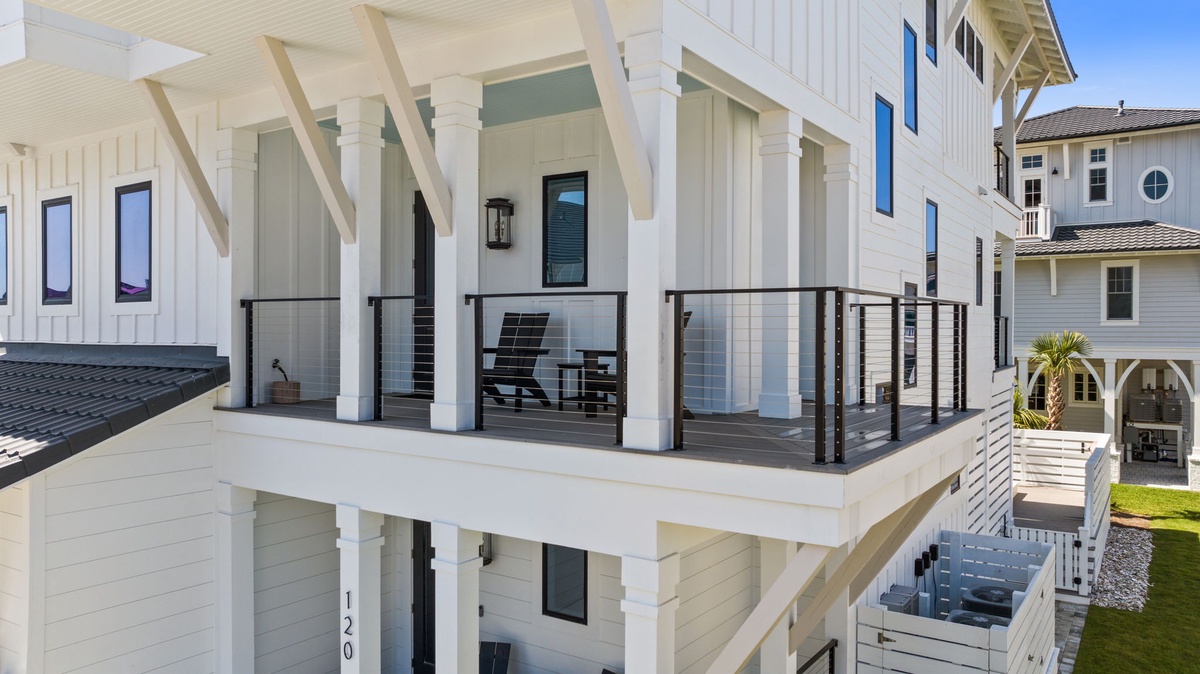 Coastal architecture frames this elevated balcony with modern metal railings and beach-style columns overlooking a quiet residential neighborhood.