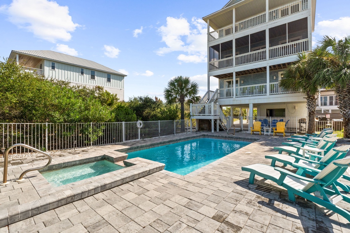 A private pool and hot tub await, surrounded by bright lounge chairs beneath swaying palms. The spacious deck offers the perfect setting for sunny days and relaxed coastal evenings.