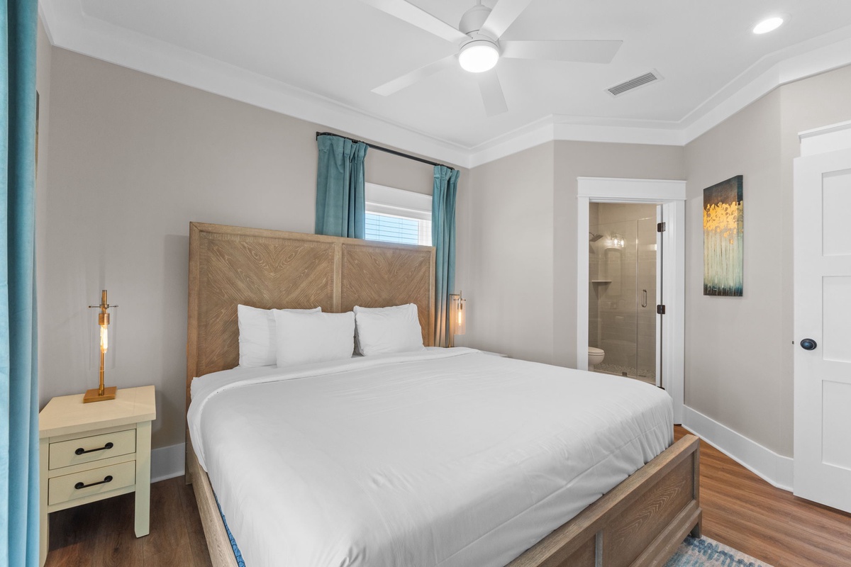Sink into crisp white linens and let the ceiling fan's gentle breeze lull you into deep, restful sleep in your serene coastal-inspired bedroom.