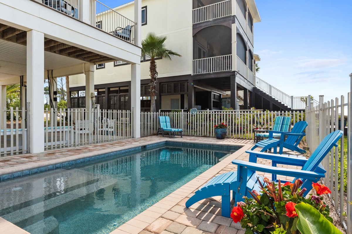 Your private pool awaits, framed by vibrant blue lounge chairs and colorful blooms. Relax under the covered patio or soak up the sun in this peaceful tropical retreat.