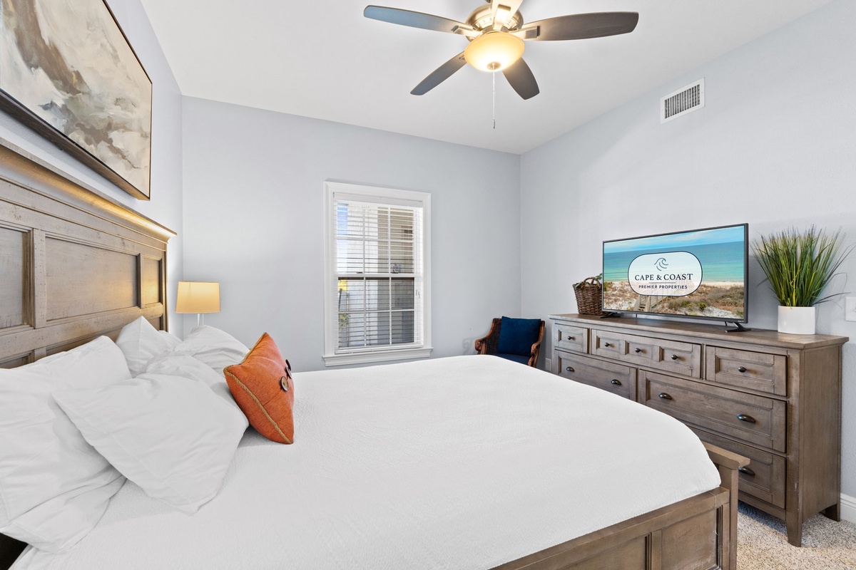 Unwind in your serene bedroom with plush bedding, ceiling fan, and entertainment center for ultimate relaxation.