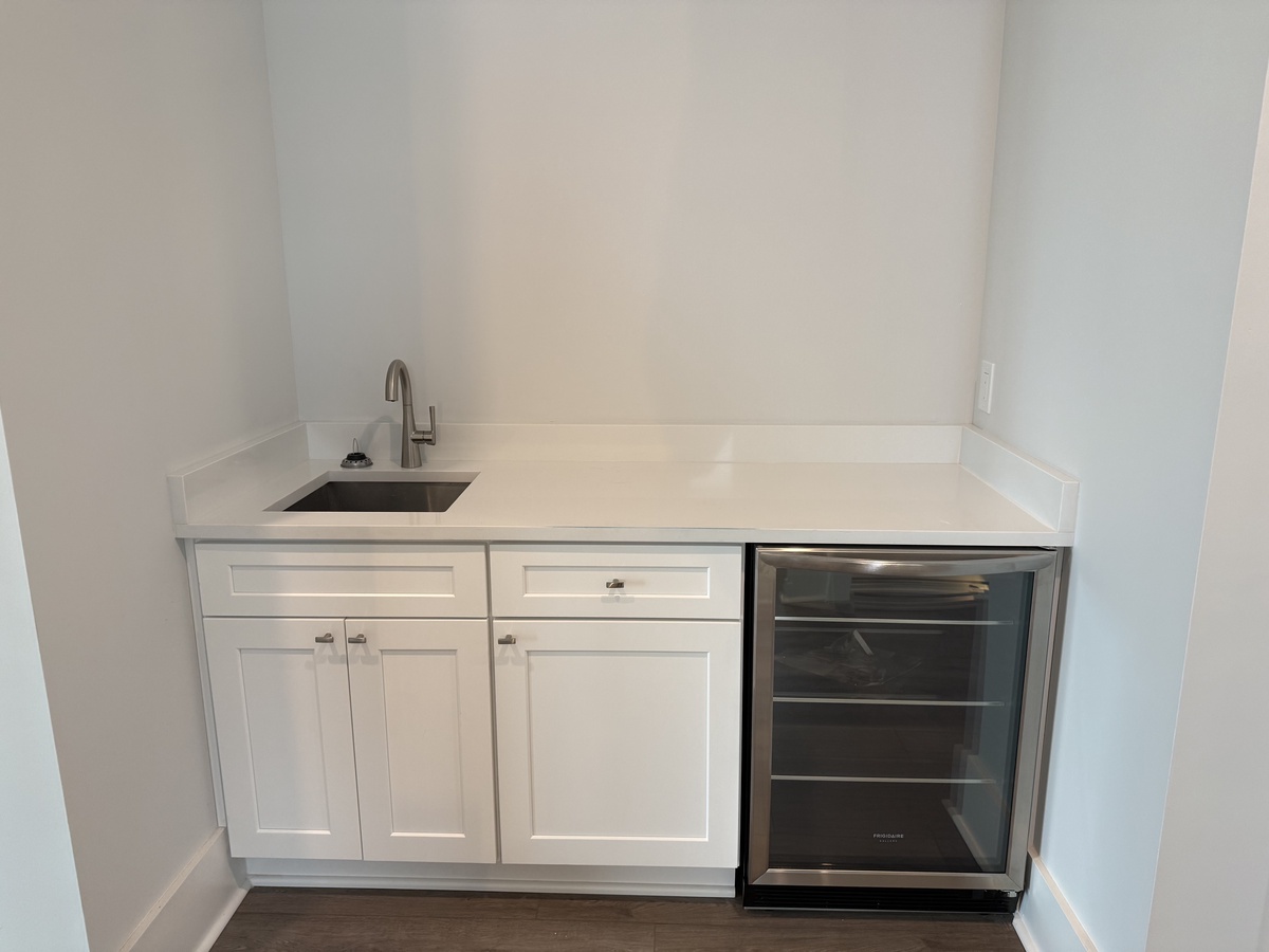Your sleek wet bar features white cabinetry, stainless steel sink, and wine fridge - perfect for entertaining in style.