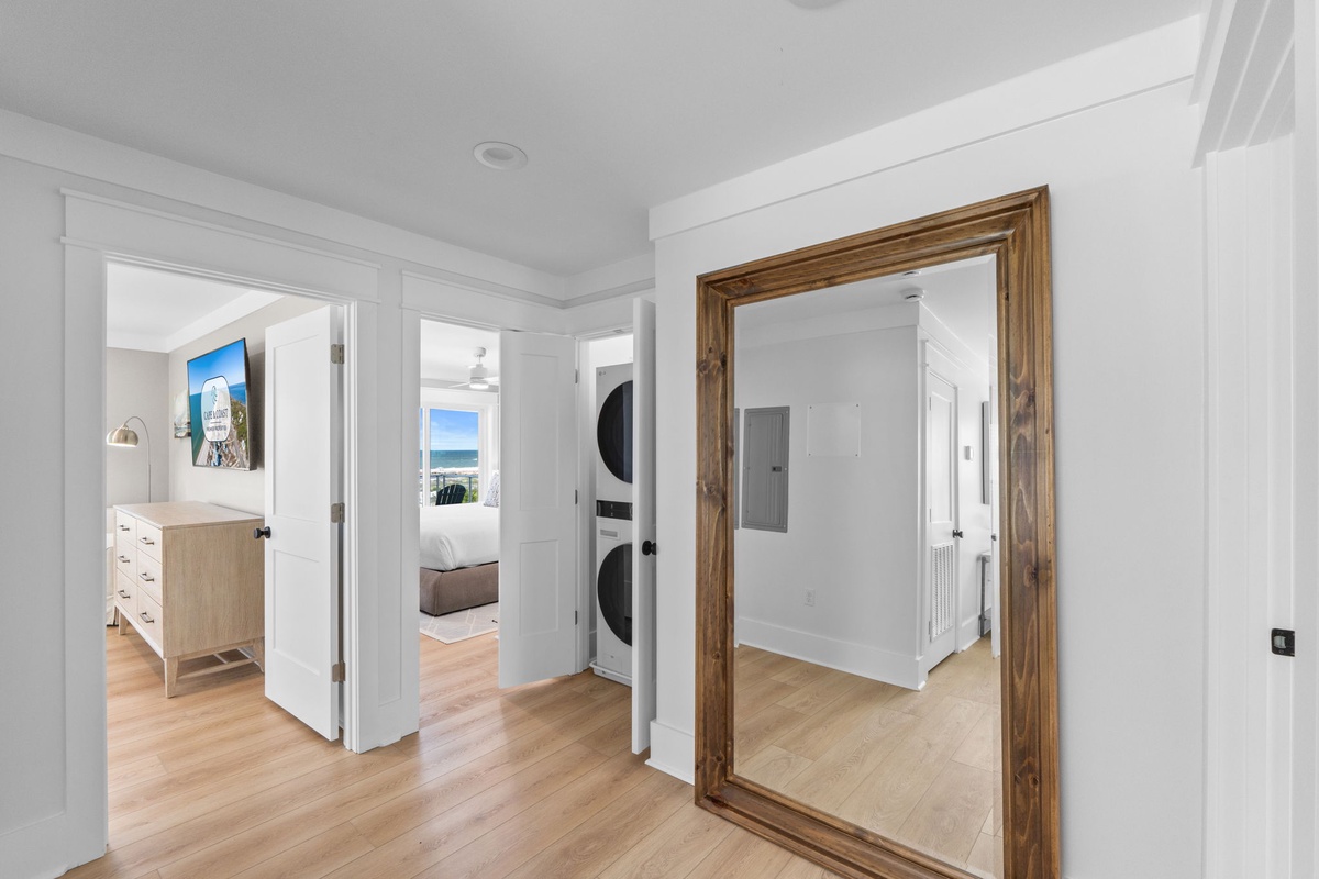 Light hardwood floors flow through this inviting hallway, connecting your bedroom and laundry. A full-length mirror adds a touch of warmth with its rustic wooden frame.