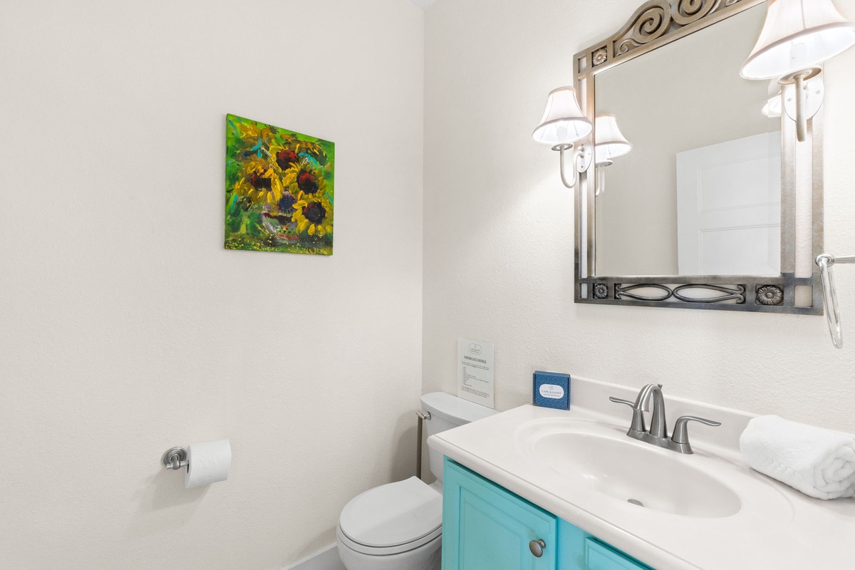 Freshen up in this bright bathroom featuring crisp white countertops, elegant mirror lighting, and cheerful sunflower artwork that adds a touch of warmth to your stay.