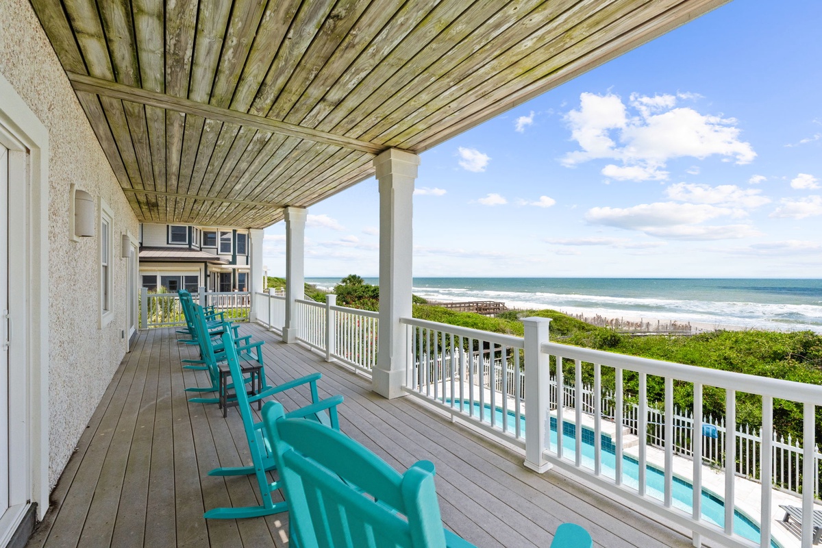 Covered porch with ocean views featuring turquoise rocking chairs, direct beach access, and lush coastal greenery—ideal for morning coffee or sunset relaxation.