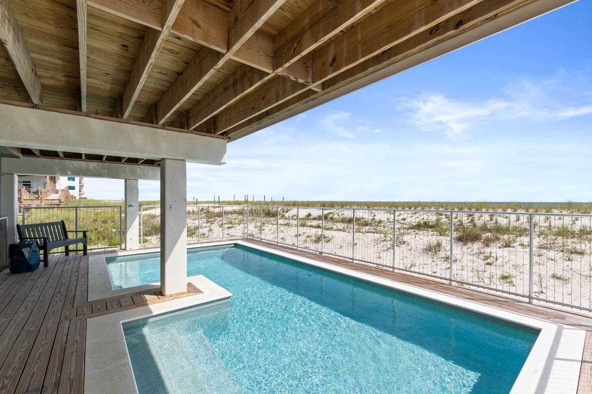 The covered pool area offers stunning coastal views across sandy dunes. A perfect spot for cooling off while taking in the beachside scenery.