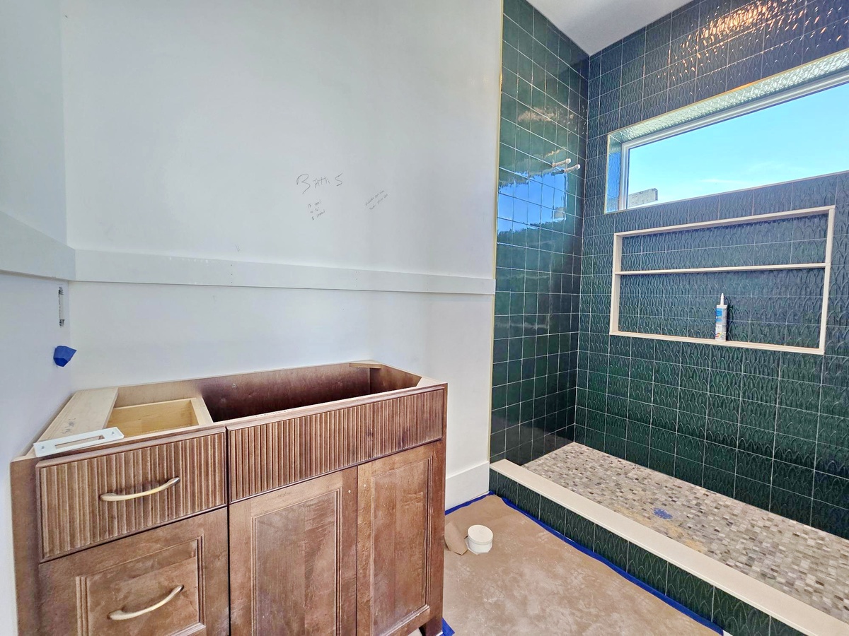 Your spacious walk-in shower features stunning emerald-green subway tile, a rainfall showerhead, and elegant built-in shelving—perfect for unwinding after a day of adventure.