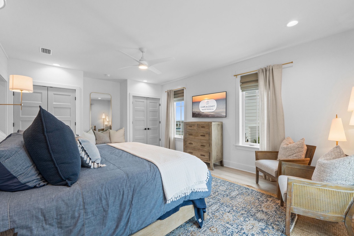 Your serene master suite features crisp blue linens, cozy seating area, and calming coastal vibes for perfect relaxation.