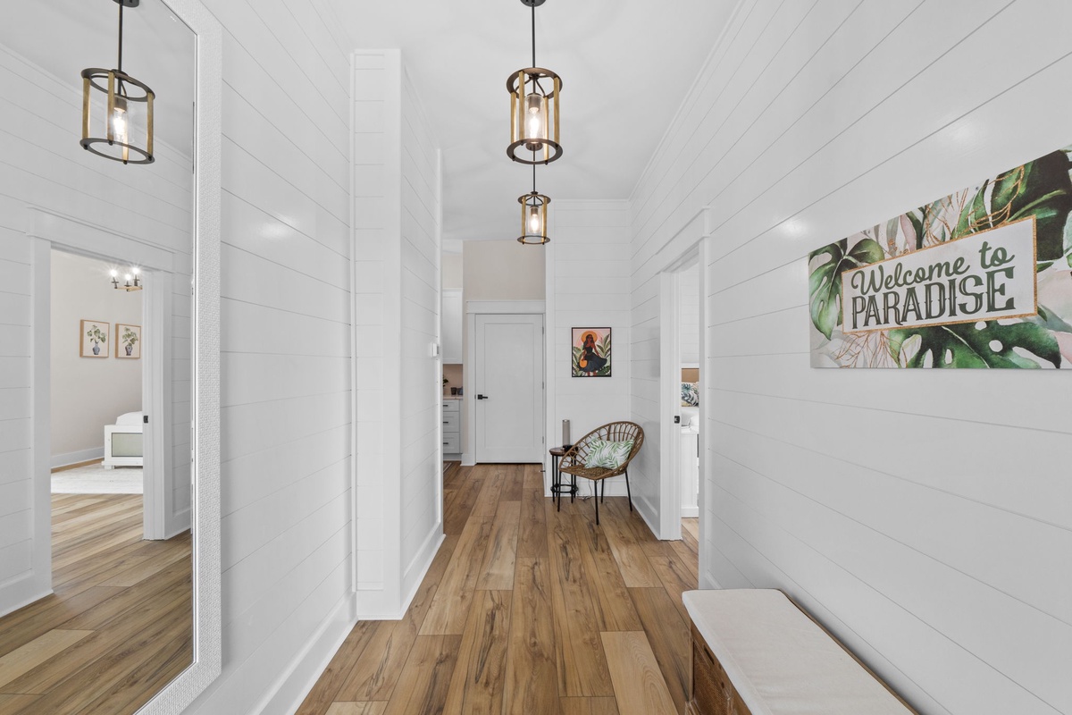 Your private paradise awaits down this bright, airy hallway with warm wood floors, charming pendant lights, and crisp white shiplap walls inviting you to explore every room.