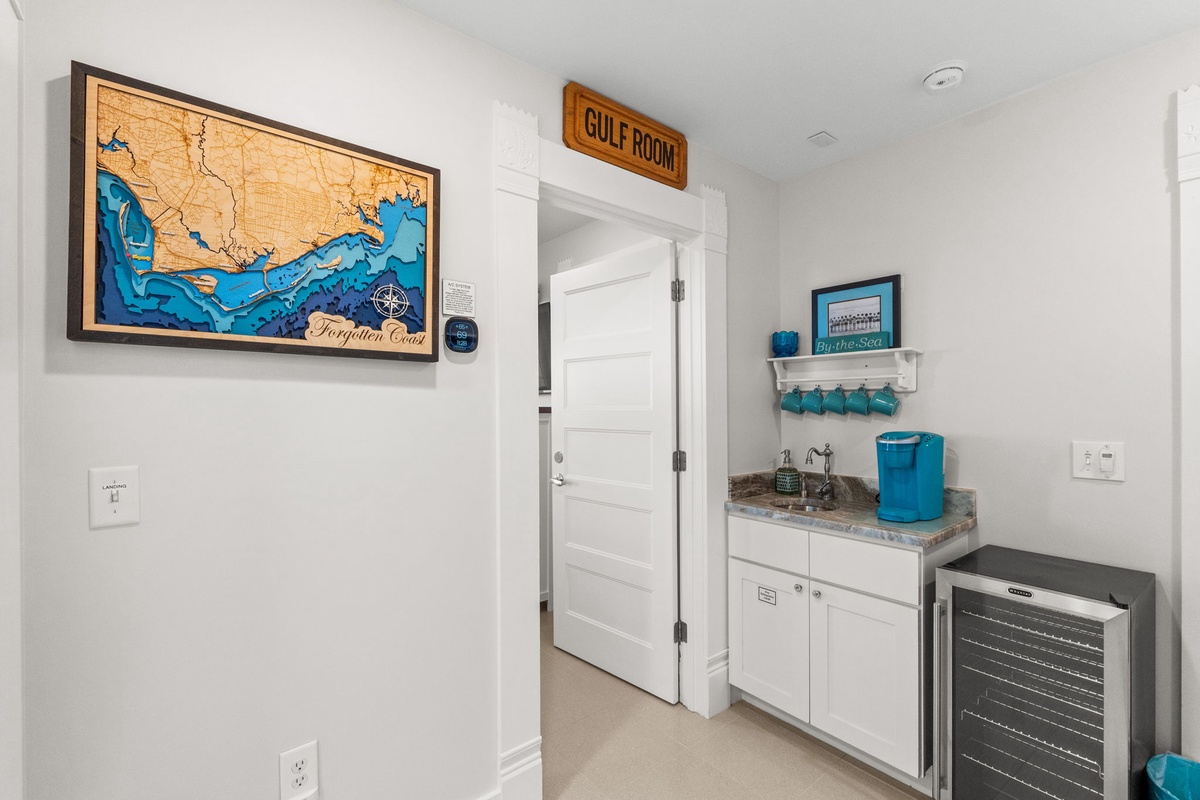 Your coastal-themed wet bar features a wine cooler and coastal artwork, perfect for mixing drinks while enjoying gulf memories.