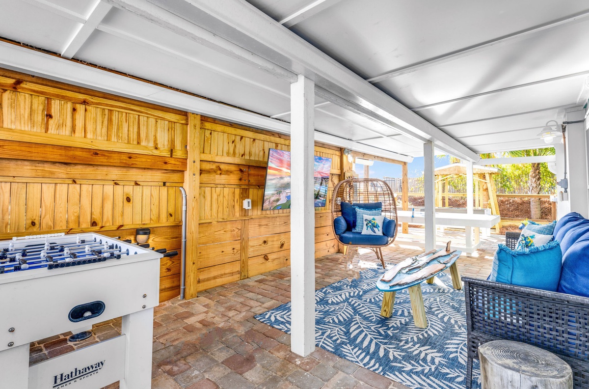 Your covered outdoor retreat features foosball, cozy seating, and a unique hanging chair—perfect for relaxing or playing games in style.