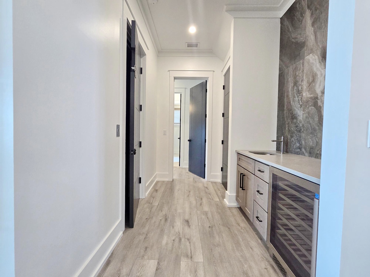 Your stylish hallway leads to multiple rooms, featuring elegant gray flooring and modern wet bar with wine fridge for evening relaxation.