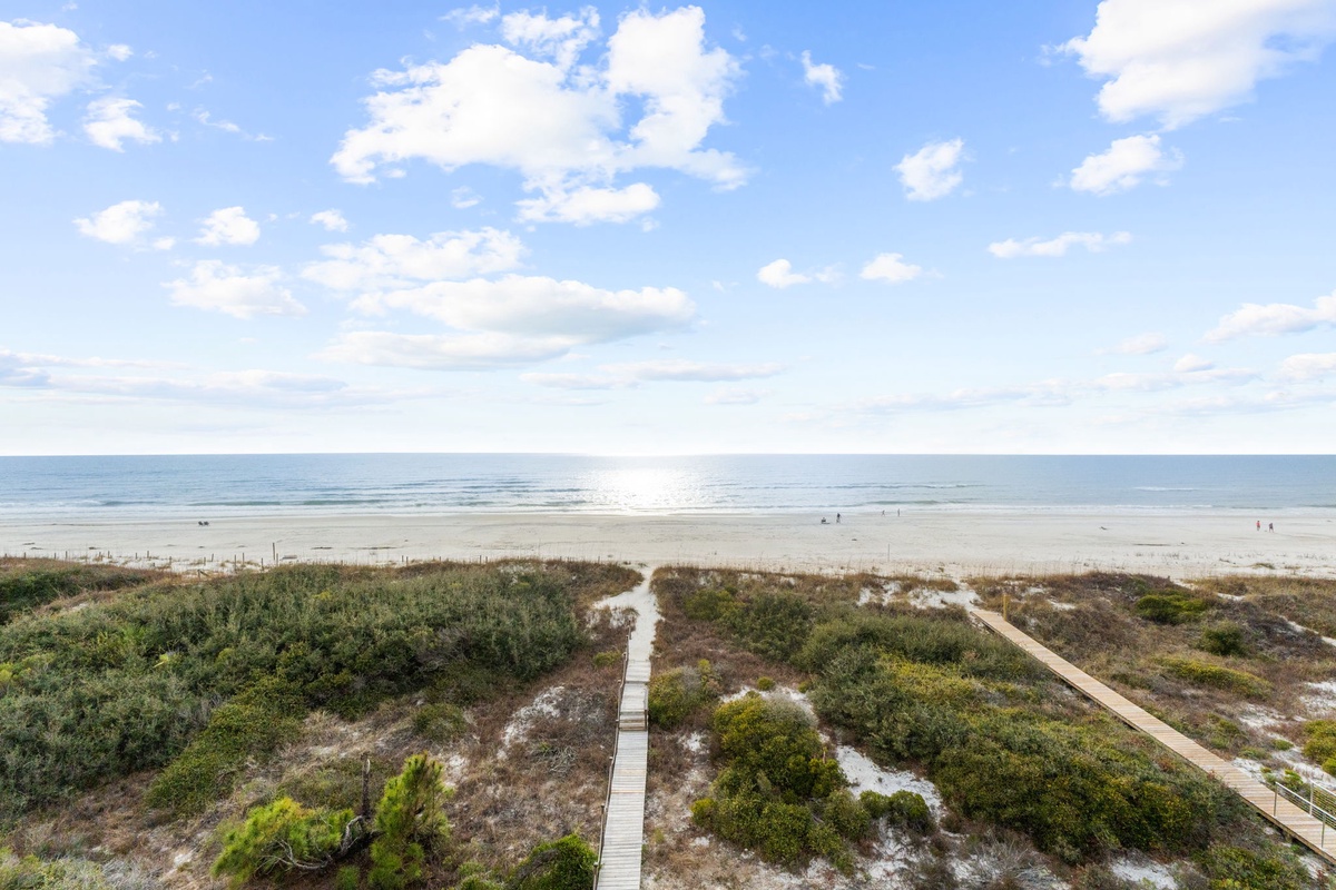 Wide sandy beach stretches along the coastline with a wooden boardwalk providing direct access through coastal dunes.