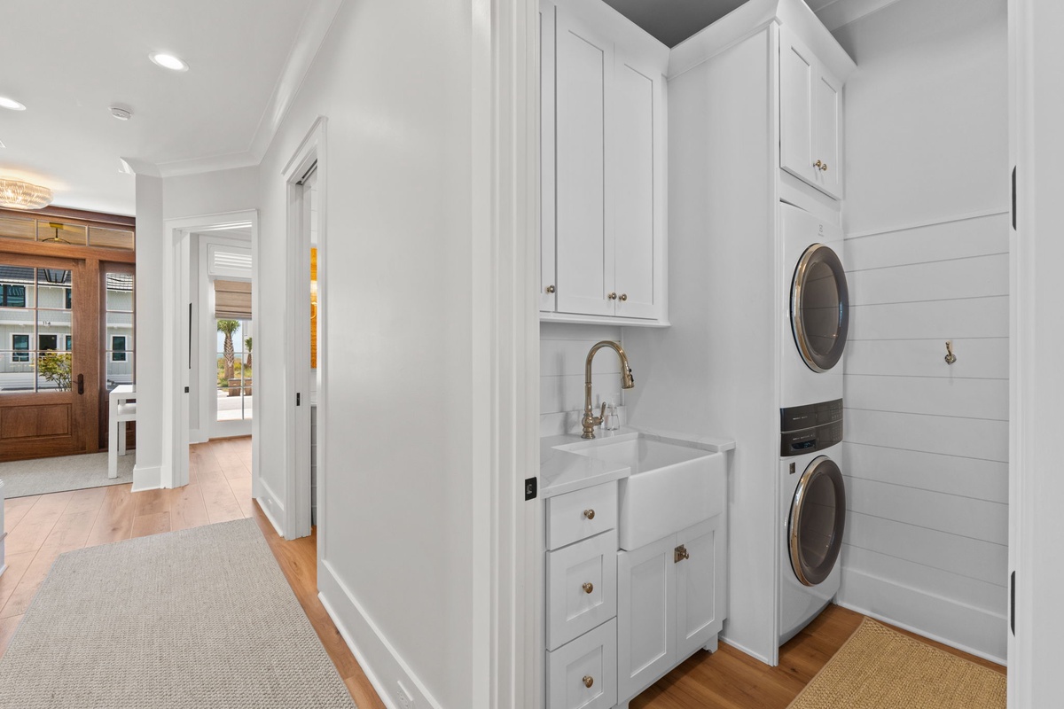 Your convenient laundry nook features modern stacked washer and dryer, pristine white cabinetry, and a farmhouse sink—making chores feel effortless in this bright, thoughtfully designed space.