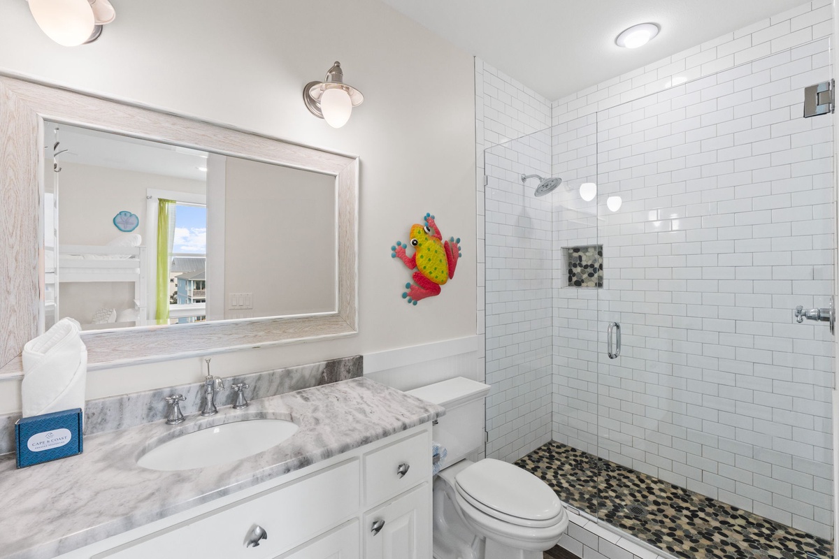 Refresh in your pristine bathroom featuring elegant marble countertops, subway tile shower, and cheerful beach-themed artwork.