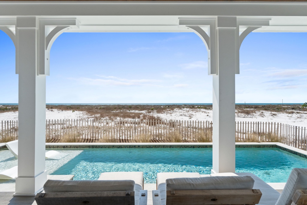 Relax on plush poolside loungers while gazing at pristine dunes and endless ocean views through elegant white columns.