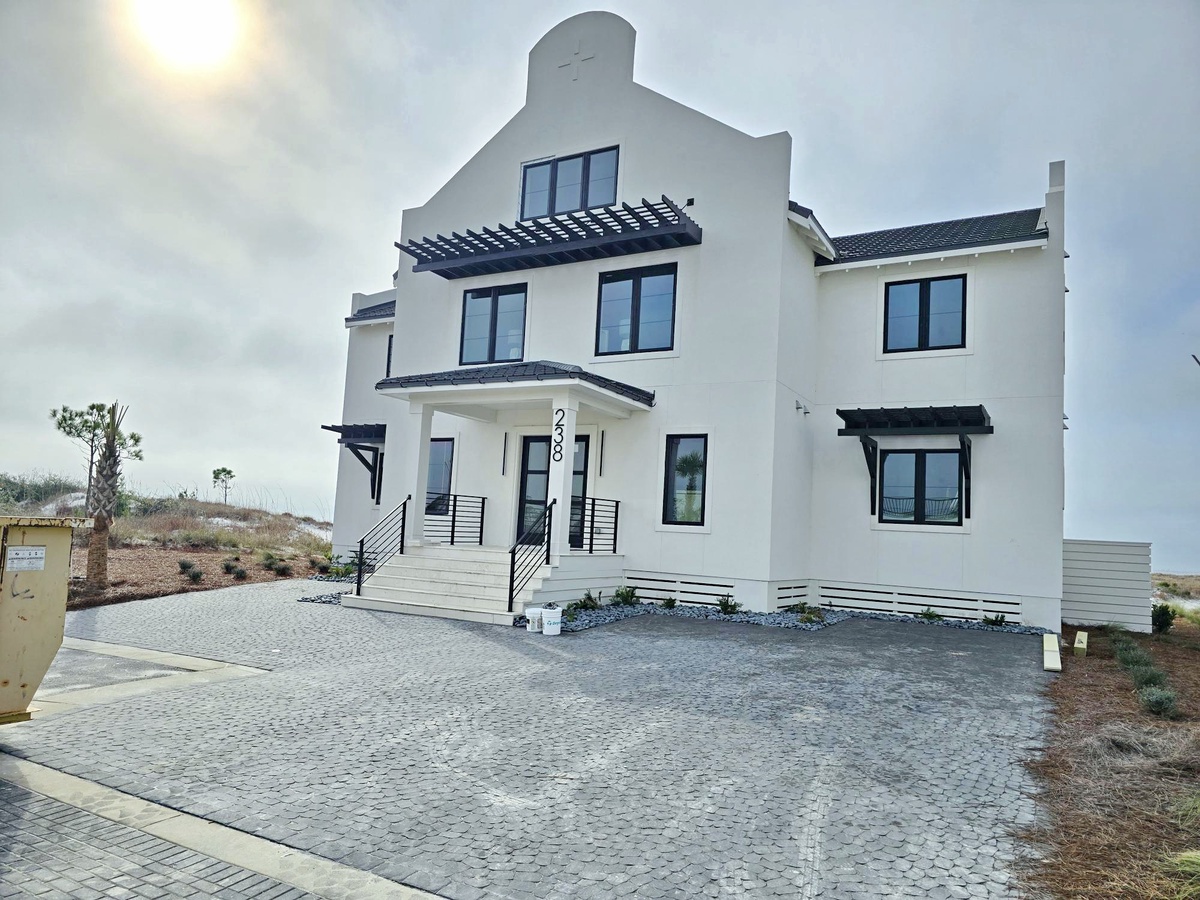 Modern white vacation home with distinctive architectural details and spacious paved courtyard for arrival and parking.