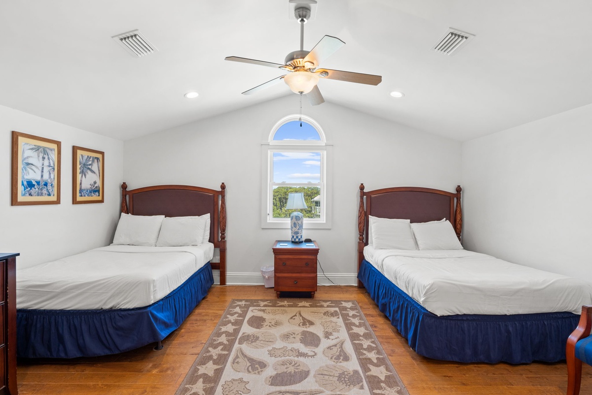 Unwind in your peaceful bedroom featuring two plush beds, vaulted ceilings, a ceiling fan, and a charming arched window framing natural light and greenery beyond.