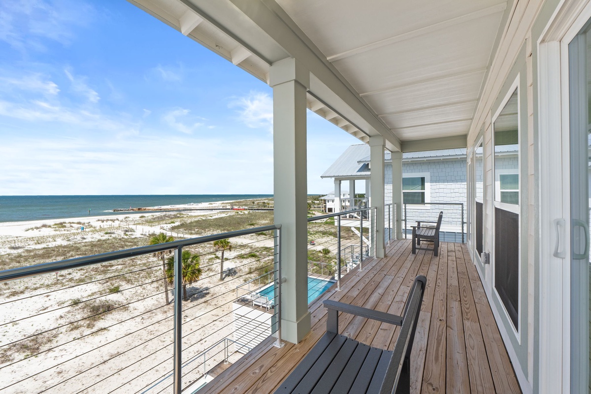 The second-story balcony overlooks white-sand shores and the open gulf, featuring a covered seating area shaded by elegant beams where you can relax with morning coffee or watch the sunset over the water.
