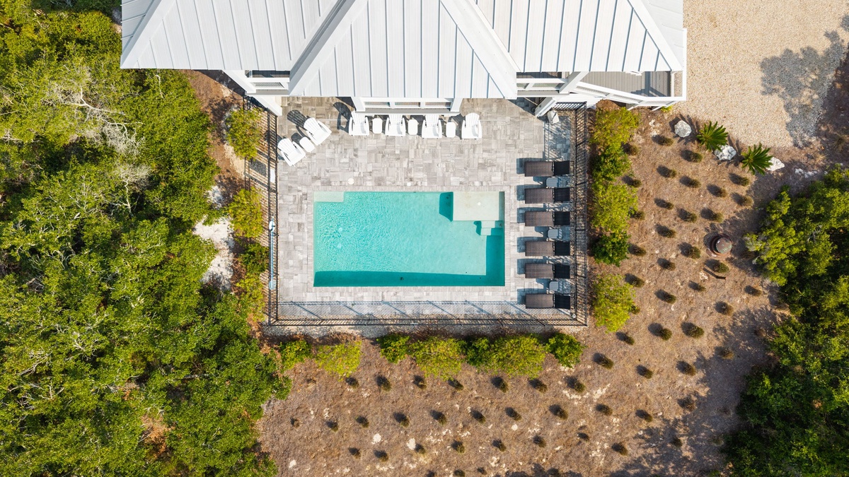 Aerial view of the property showcasing a sparkling pool surrounded by lush greenery and elegant outdoor patio spaces.