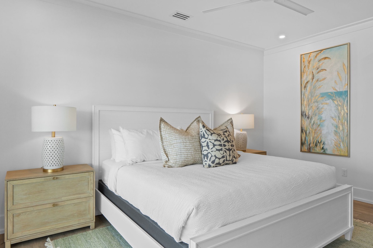 Slip into this serene bedroom where crisp linens and coastal artwork create your peaceful retreat. Soft lighting and thoughtful design invite restful nights and easy mornings.