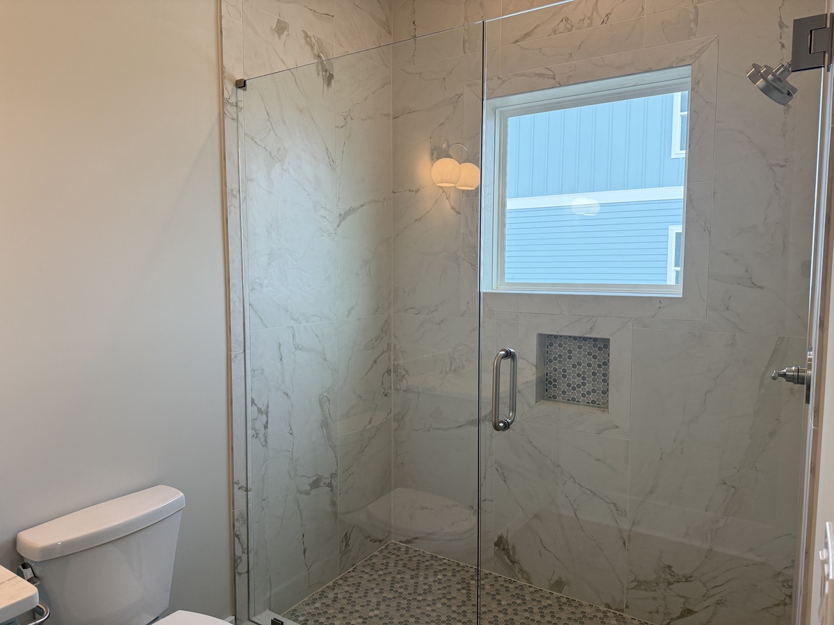 Step into your spa-like marble shower featuring elegant glass doors and natural light from the window above.