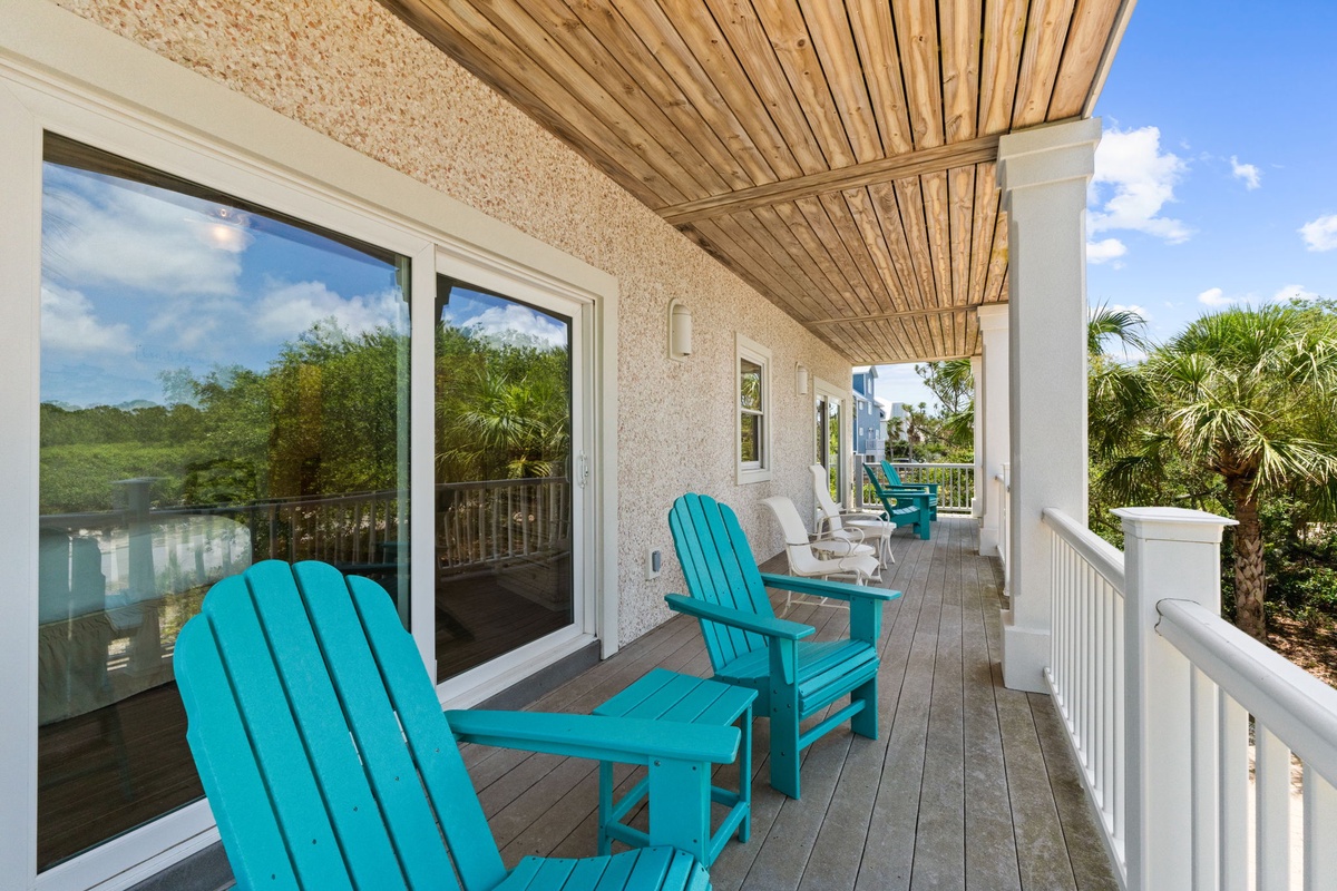 A covered deck with turquoise Adirondack chairs overlooks lush tropical vegetation and tranquil waterfront views. Perfect for morning coffee or evening relaxation.