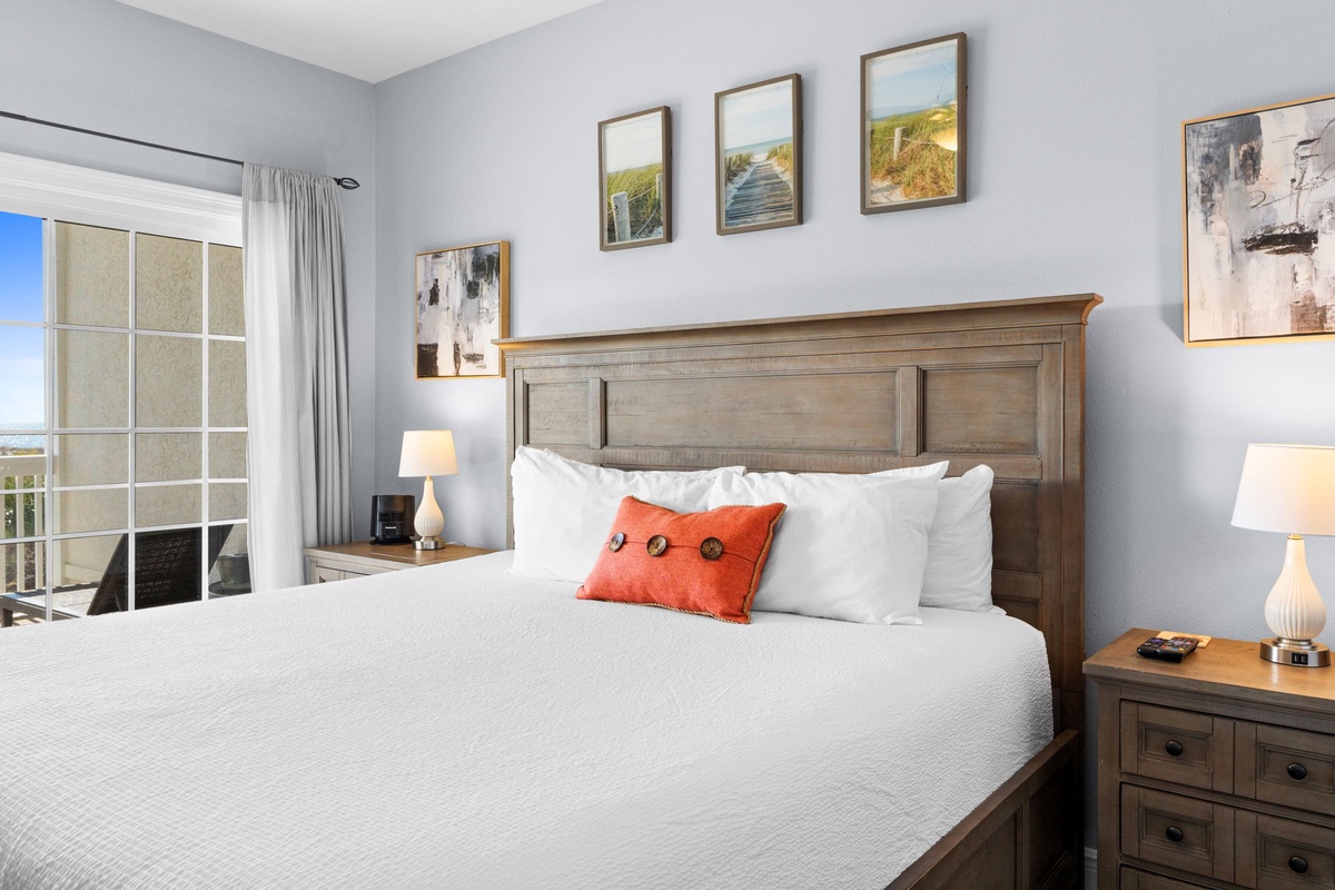 Sink into crisp white linens and unwind in this serene bedroom, where coastal artwork and warm wood accents create your perfect retreat.