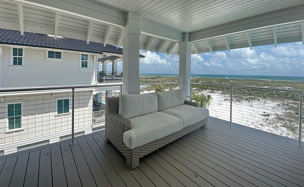 Covered deck with cushioned seating overlooking pristine coastal dunes and turquoise ocean—perfect for morning coffee or sunset cocktails in complete comfort.