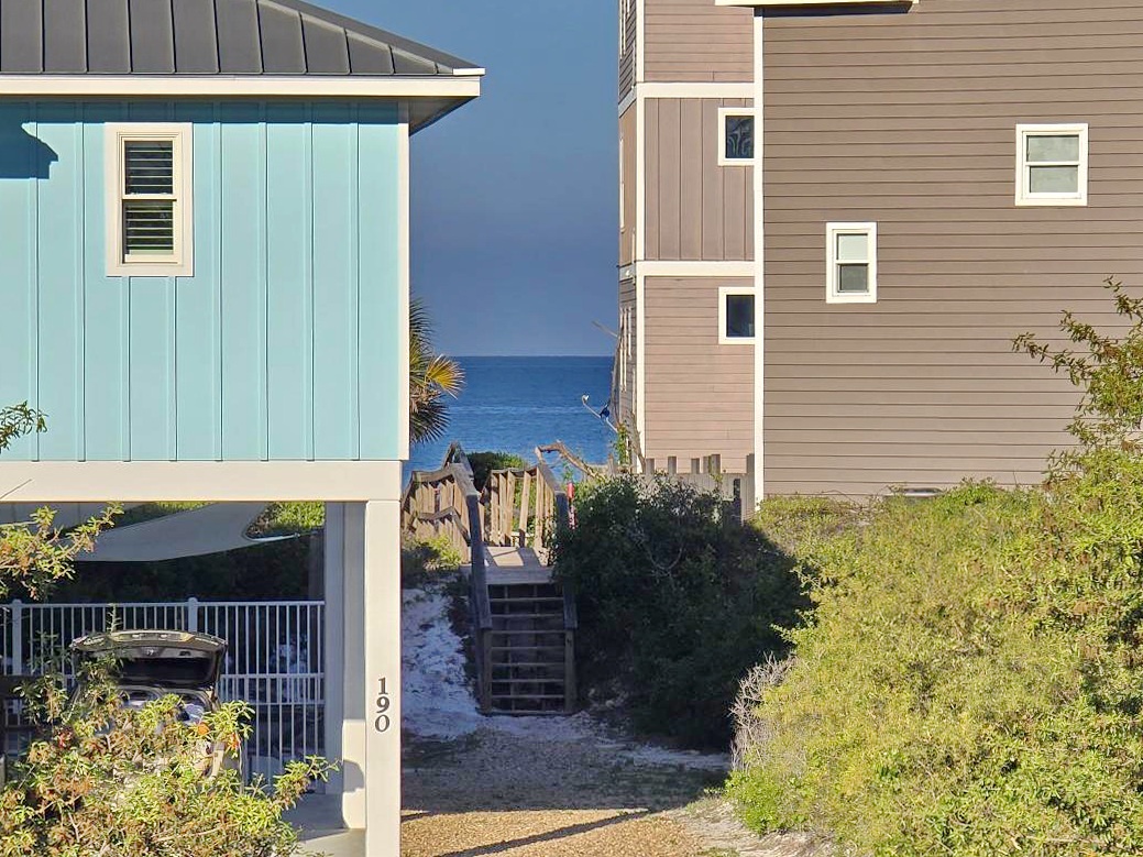 Charming coastal homes with a scenic wooden boardwalk leading directly to pristine sandy shores and sparkling blue waters.