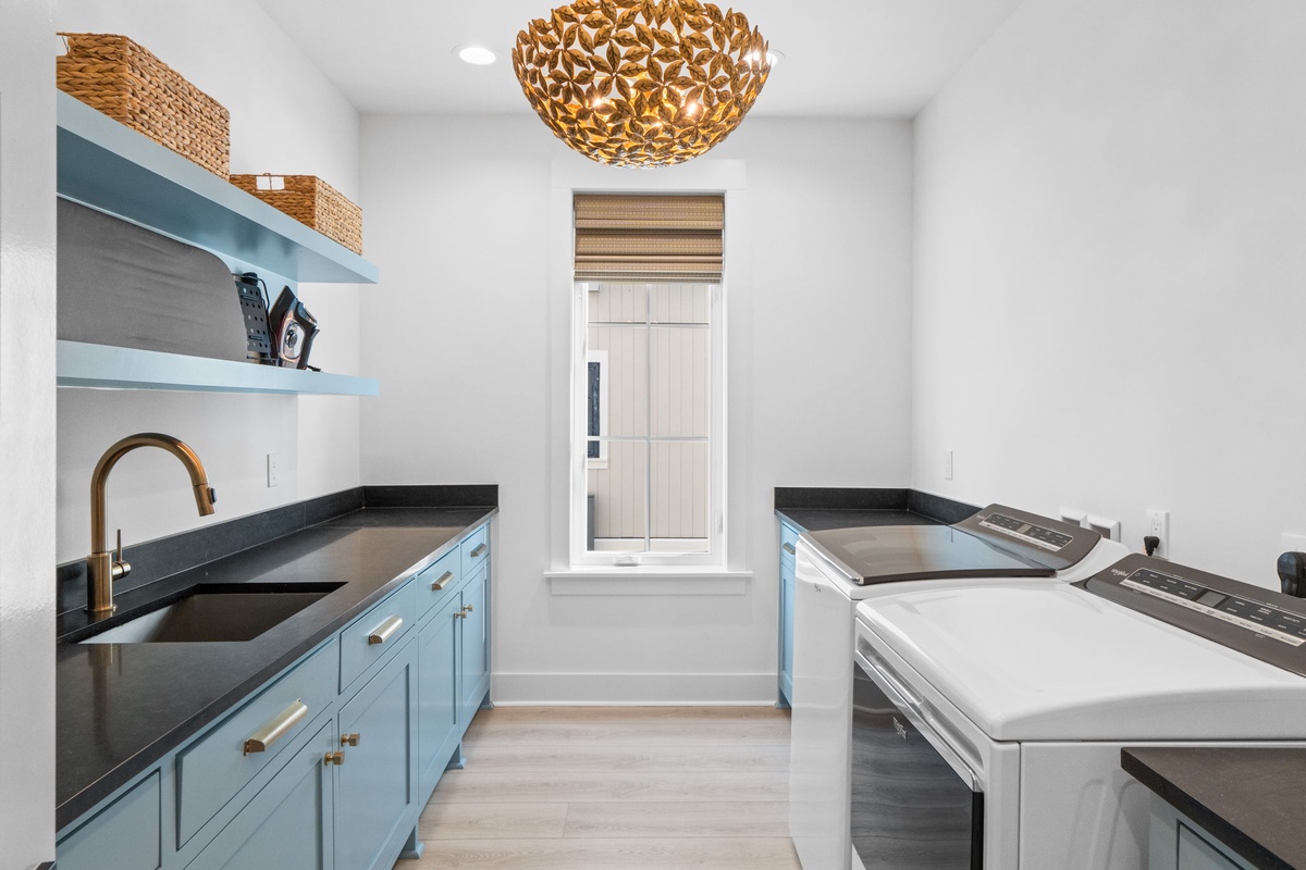 Prepare your favorite meals in this stylish kitchen featuring beautiful blue cabinetry, sleek countertops, and a stunning gold pendant light overhead.