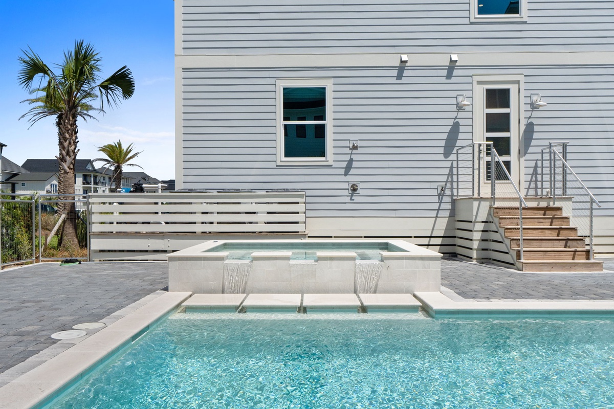 Sparkling pool with built-in fountain features and spacious deck surrounded by swaying palms—your private oasis awaits under sunny skies.