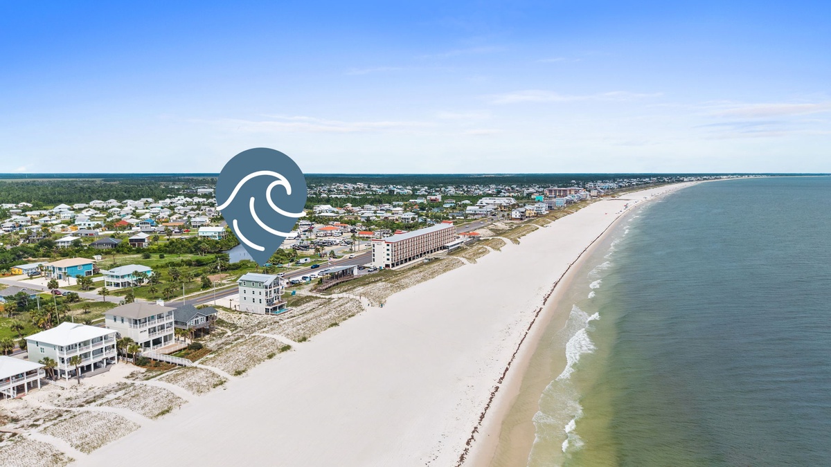 Aerial view captures a pristine white-sand beach stretching along turquoise waters, with the property nestled among coastal residences, offering easy access to the shore and stunning seaside surroundings.