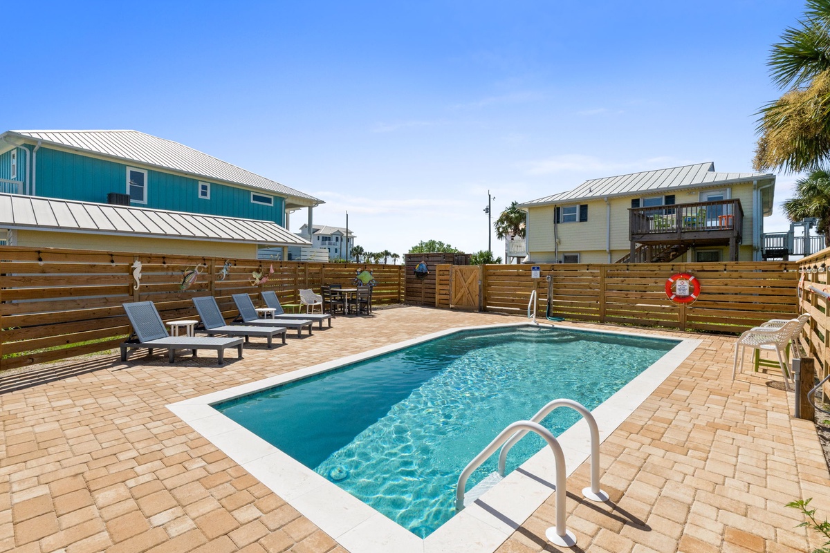 Dive into your own private pool surrounded by sunny pavers and comfy lounge chairs, perfect for unwinding under clear blue skies in this coastal retreat.