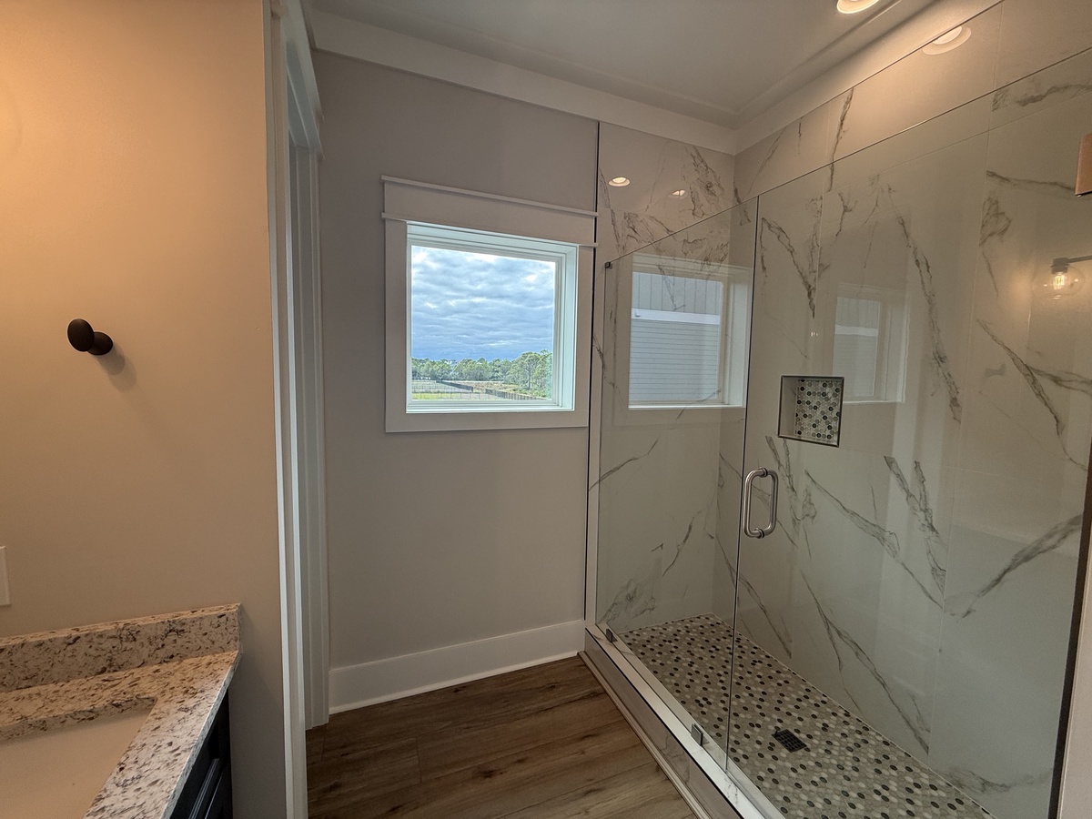 Step into your luxurious marble-clad shower with glass doors, where natural light filters through the window as you unwind in this spa-like retreat.