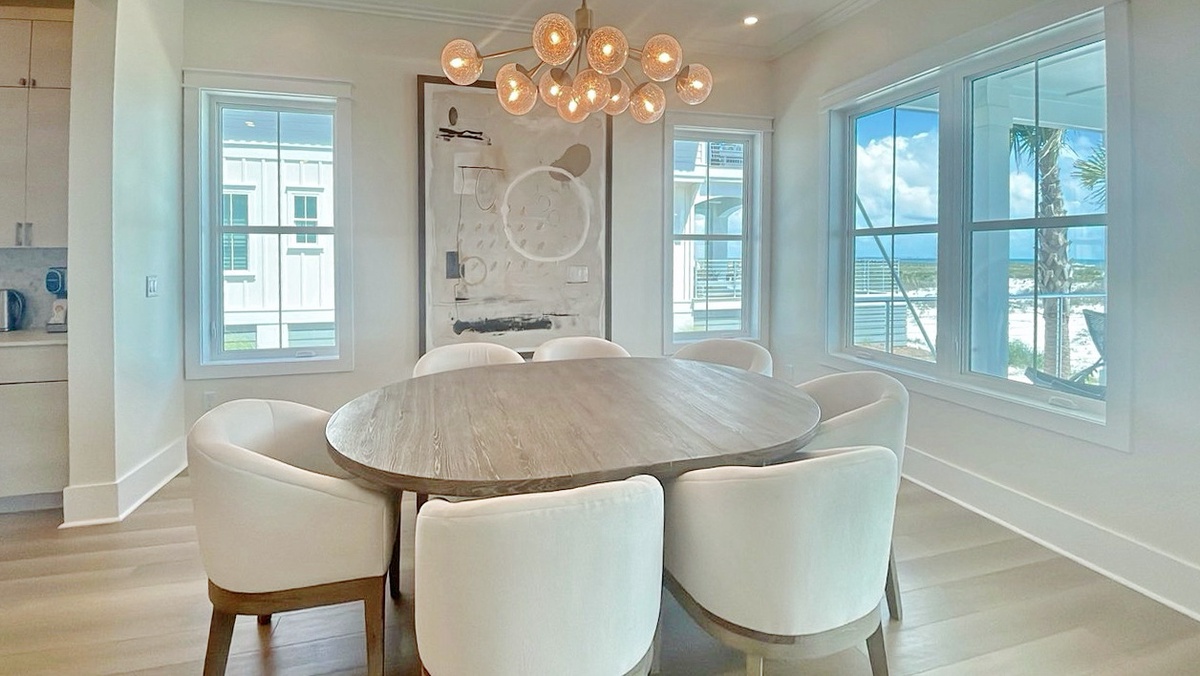 Gather around this elegant dining table, where coastal views and natural light create the perfect backdrop for your meals together, complemented by a stunning chandelier overhead.