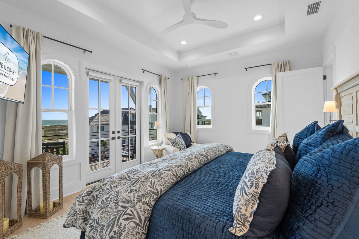 Drift off in this serene bedroom where plush blue bedding meets elegant arched windows framing coastal views.
