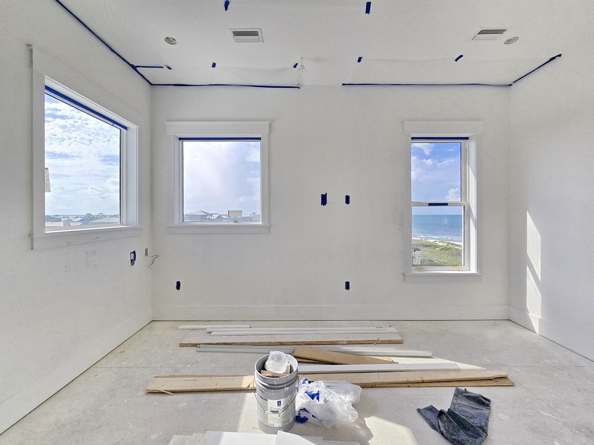 A bright, unfinished room awaits your personal touch, with stunning ocean views visible through large windows—a serene coastal backdrop for your upcoming vacation.