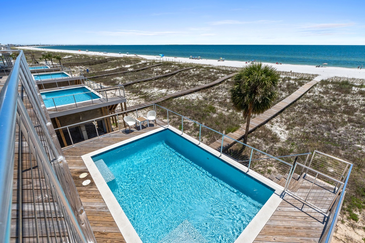 Stunning elevated view captures the property's private pool deck overlooking pristine white sand beaches and crystal-clear turquoise waters, with convenient boardwalk access leading directly to the shore.
