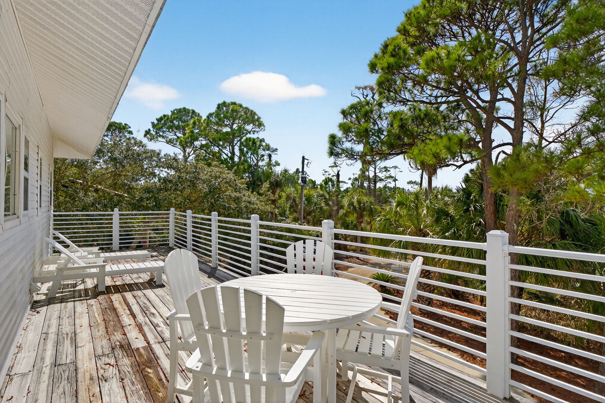 Relax on your private deck with white outdoor furniture, surrounded by lush tropical trees and clear blue skies.