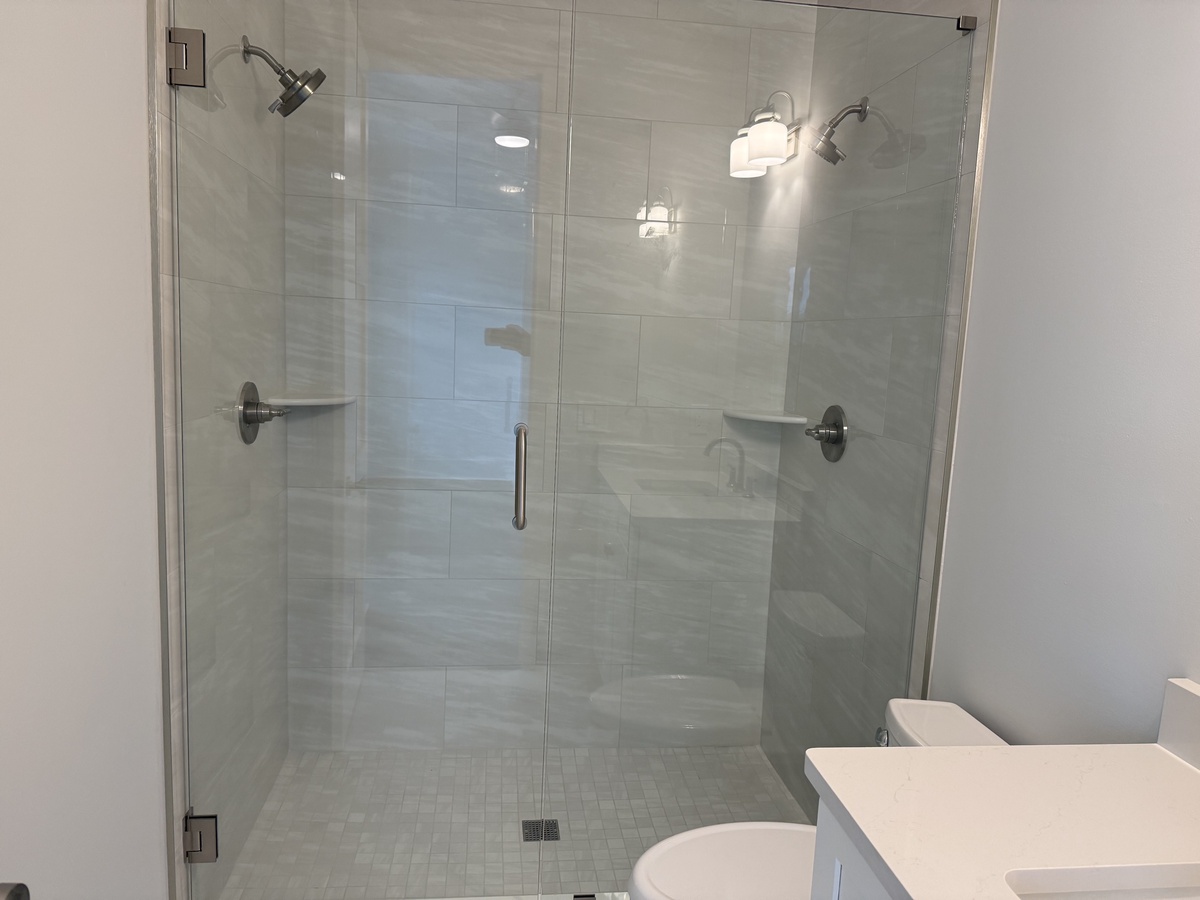 Step into your luxurious glass-enclosed shower with dual rainfall heads and built-in seating for a spa-like experience.