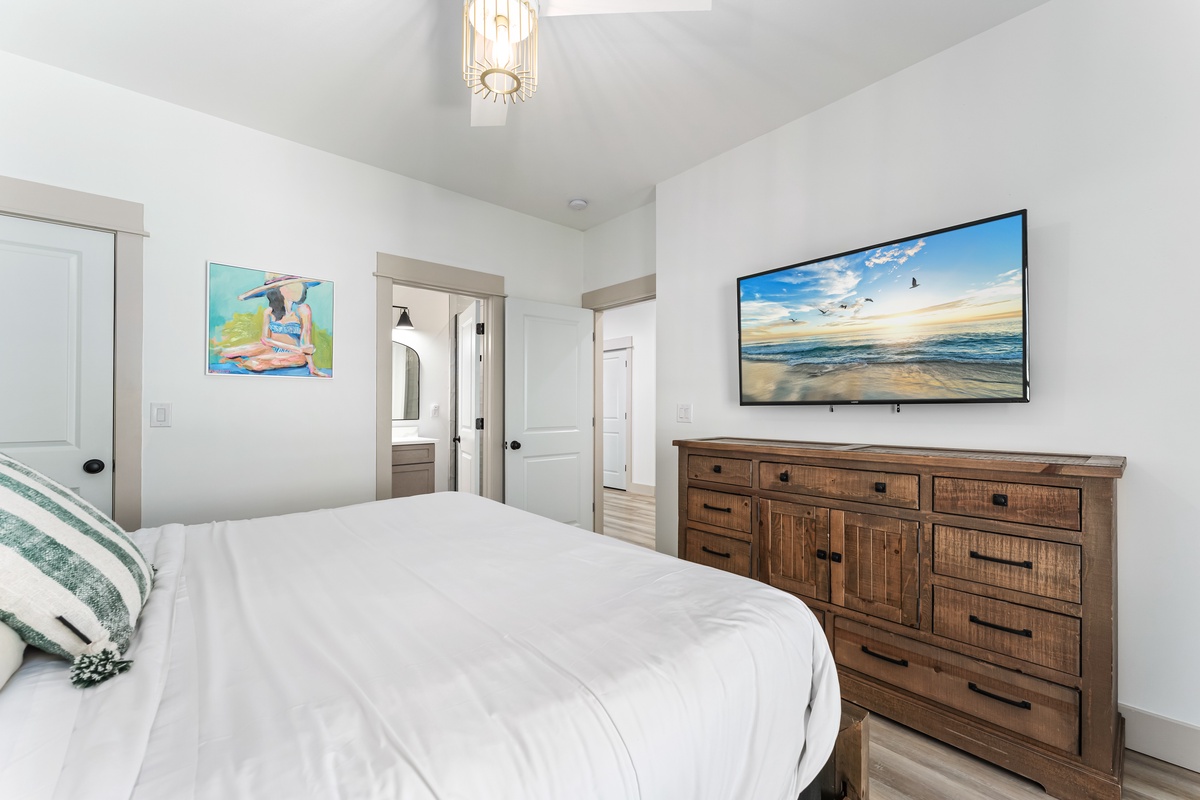 Relax in your serene bedroom with crisp linens, rustic wood dresser, and wall-mounted TV for cozy nights in.