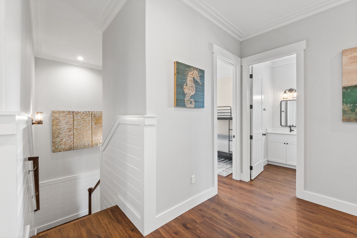 Step into your welcoming upstairs hallway, where coastal artwork and warm wood floors create a peaceful retreat atmosphere.