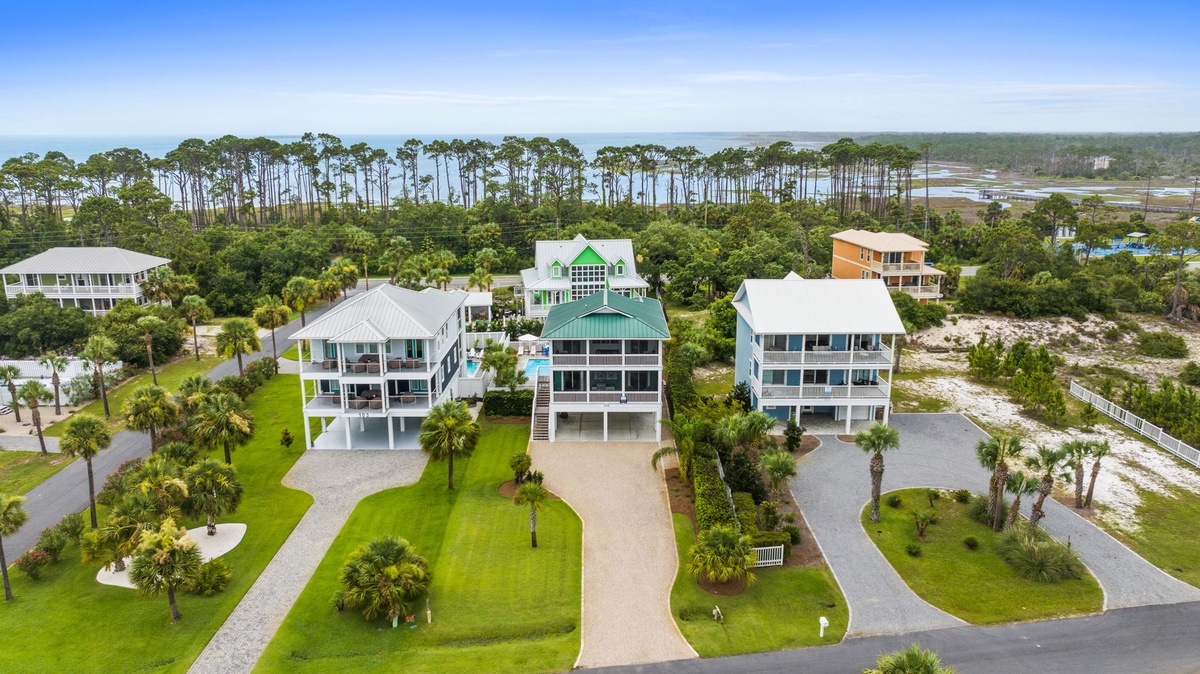 Aerial view showcasing the coastal vacation rental neighborhood, surrounded by lush landscaping and natural wetlands, with neighboring properties offering a peaceful beachside setting.
