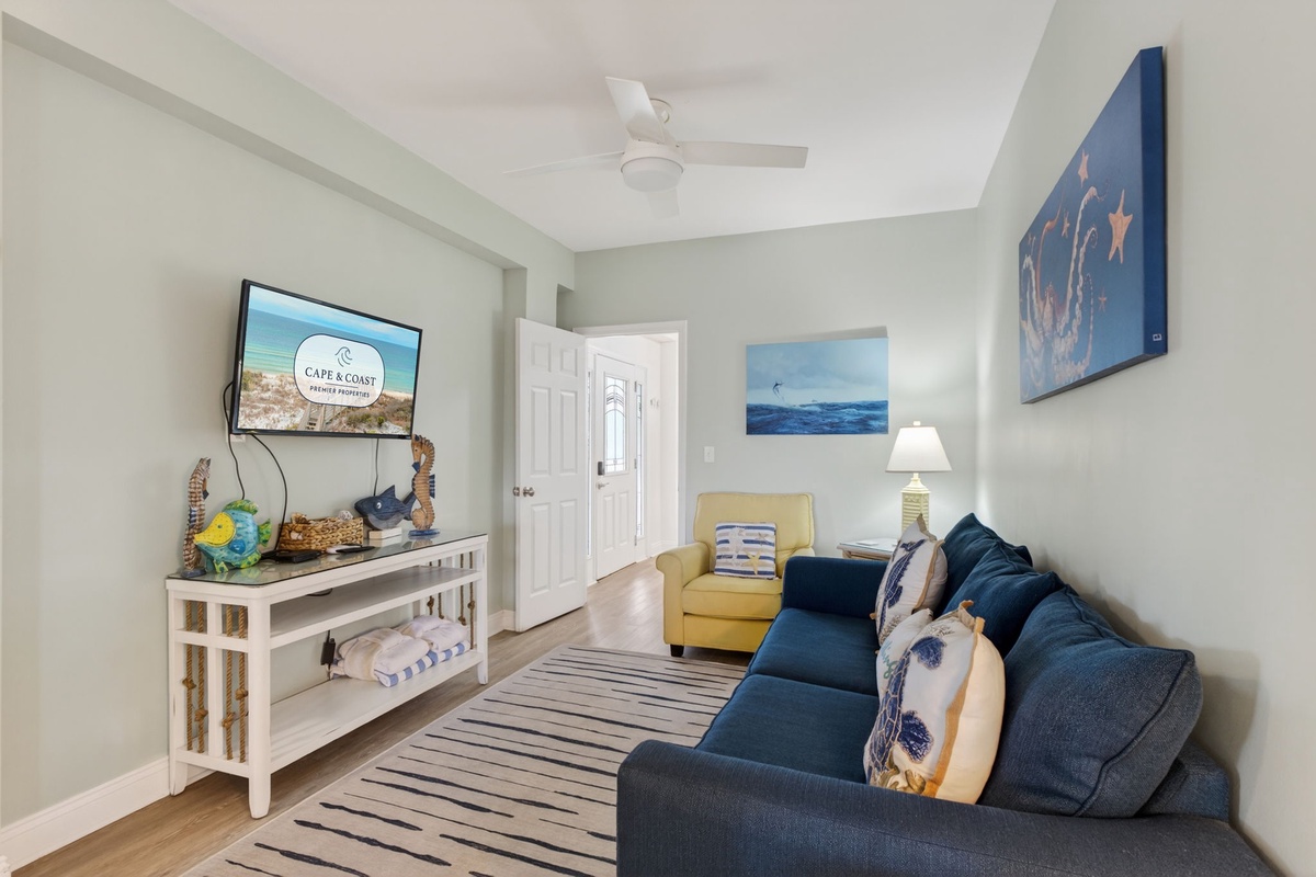 Relax in your coastal-themed living room with ocean artwork, comfy seating, and entertainment center for perfect vacation evenings.