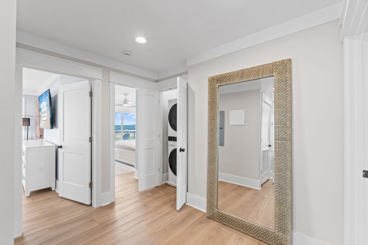 Thoughtfully designed hallway with convenient laundry access and a coastal-chic mirror. Peek through the doorway to catch a glimpse of your beachfront escape waiting just beyond.