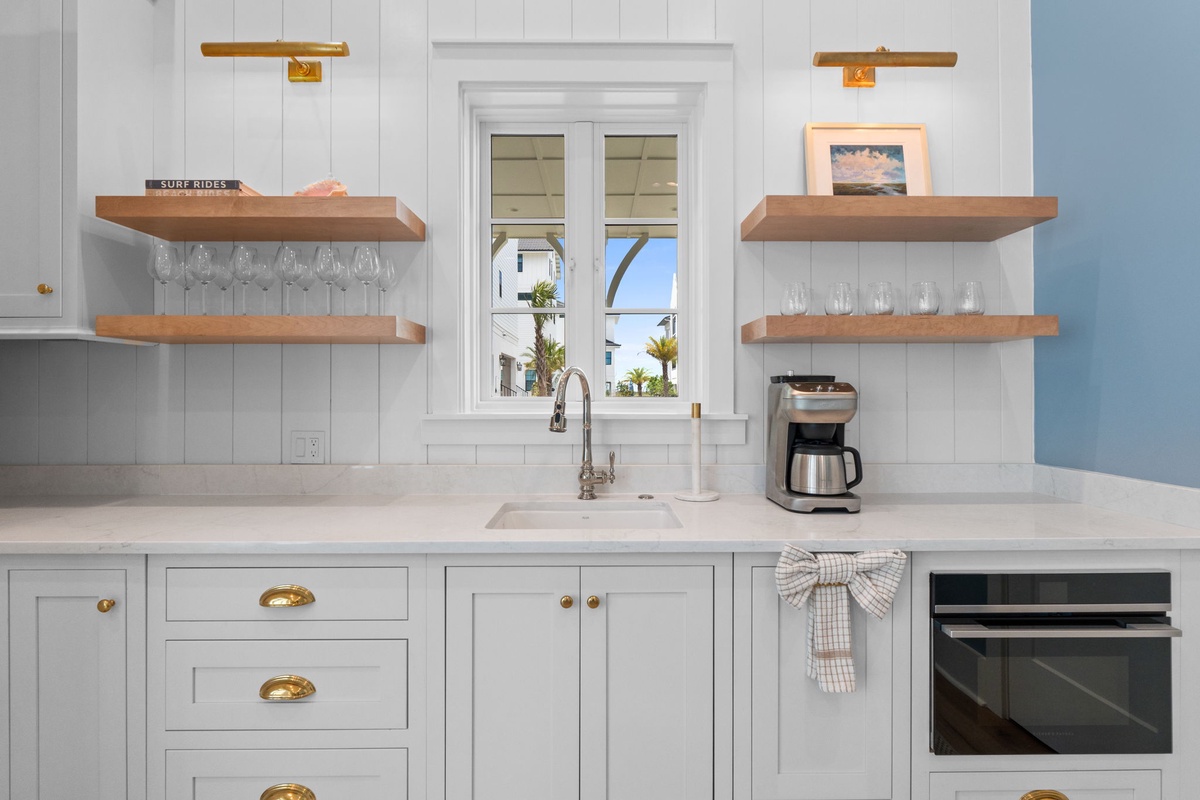 Your bright, fully-equipped kitchen features coastal charm with open shelving, fresh white cabinetry, and a coffee maker ready for your morning brew.